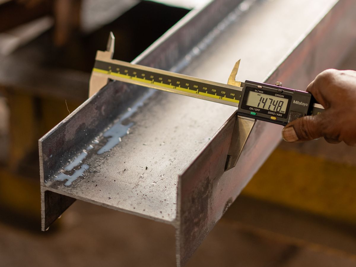 A machined steel section being checked with a digital caliper